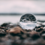 A glass ball reflecting water by the shore